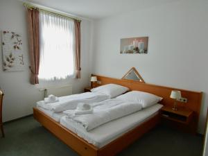 a bedroom with a bed with white sheets and a window at Pension Hexenkessel in Wernigerode