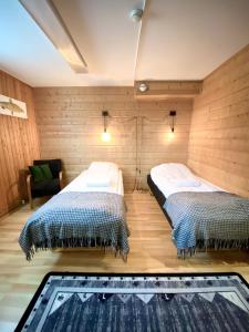 two beds in a room with wooden walls at Lumi Guest House in Arvidsjaur