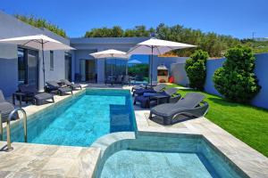 a swimming pool with chairs and umbrellas next to a house at Villa Zaneti by PosarelliVillas in Agia Marina Nea Kydonias