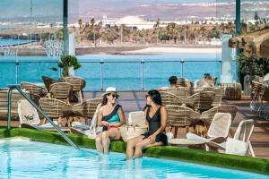 two women sitting in a swimming pool at a resort at Arrecife Gran Hotel & Spa in Arrecife