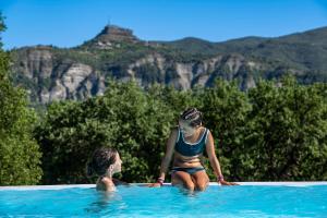 Duas raparigas estão sentadas numa piscina. em Charmant camping Familiale 3 Etoiles vue 360 plage piscine à débordement empl XXL em Labeaume