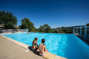 duas mulheres sentadas à beira de uma piscina em Charmant camping Familiale 3 Etoiles vue 360 plage piscine à débordement empl XXL em Labeaume