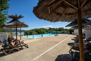a group of people sitting in chairs next to a swimming pool at Charmant camping Familiale 3 Etoiles vue 360 plage piscine à débordement empl XXL in Labeaume
