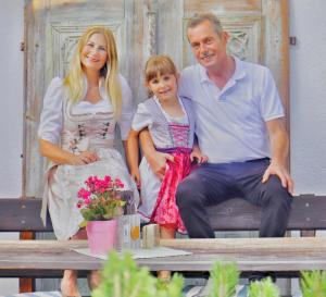 Ein Mann und eine Frau sitzen auf einer Bank mit einem kleinen Mädchen in der Unterkunft Gasthof Enzian in Tannheim