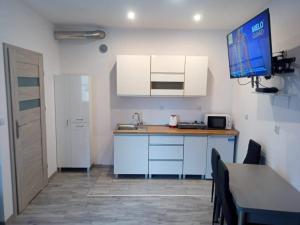 a kitchen with white cabinets and a television on the wall at Apartament Po schodkach in Duszniki Zdrój