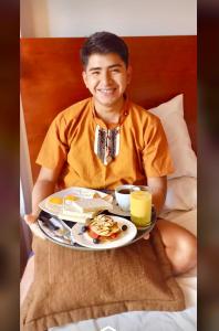 a young man sitting in bed with a plate of food at Victtorios Hotel in Satipo