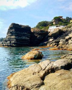 a body of water with rocks and a house on a hill at Hotel La Scogliera in Cavi di Lavagna