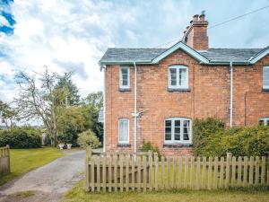 a brick house with a wooden fence in front of it at Eudon Burnell Cottage in Eardington