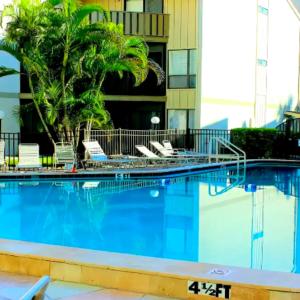 a swimming pool with chairs and palm trees in front of a building at Sarasota Pool Apartment in Siesta Key