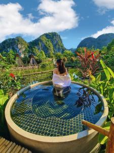 a woman sitting in a pool with mountains in the background at Trang An Lamia Bungalow in Ninh Binh