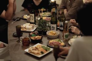 un grupo de personas sentadas alrededor de una mesa con comida y vino en Good Neighbors, en Kanazawa