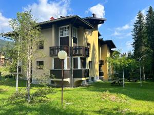 a yellow house with a balcony and a yard at Cosy Lodge in Madonna di Campiglio