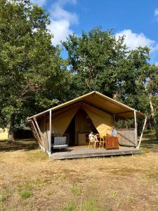 une tente avec un chien assis sur une terrasse couverte dans l'établissement Camping la Kahute, tente lodge au coeur de la forêt, à Carcans