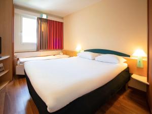 a hotel room with a large white bed and a window at ibis Fribourg in Fribourg