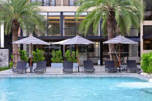 uma piscina com cadeiras e guarda-sóis e palmeiras em BS Residence Suvarnabhumi - SHA Extra Plus em Lat Krabang