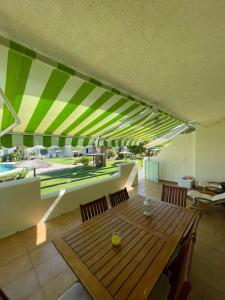 a dining room with a wooden table and green and white awnings at Casa adosada con porche, piscina y pista de pádel, junto al campo de golf in El Portil