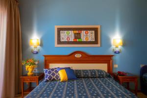 a bedroom with a blue wall with a bed and two lamps at Hotel Riva Del Sole in Cefalù
