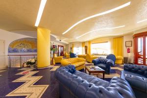 a living room with blue couches and yellow chairs at Hotel Riva Del Sole in Cefalù