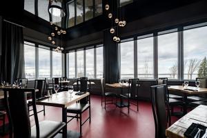 un restaurante con mesas, sillas y ventanas grandes en Hotel de la Rive, en Sorel