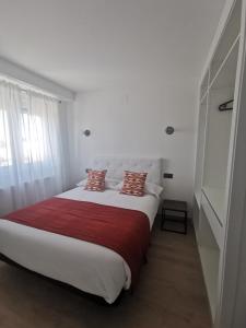 a white bedroom with a large bed with red blanket at Apartamentos Seijo in Villalba