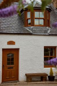 a white building with a wooden door and a bench at Crossroads Cottage in Drumnadrochit