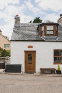 - un bâtiment blanc avec une porte en bois et un banc dans l'établissement Crossroads Cottage, à Drumnadrochit