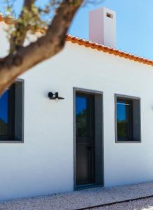 uma casa branca com uma porta preta e janelas em Monte da Fonte na Zambujeira do Mar