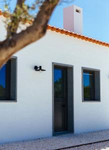 a white house with a black door and windows at Monte da Fonte in Zambujeira do Mar