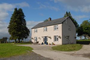 una casa blanca con una mesa y un árbol en Coolbeg Farmhouse, en Maguires Bridge