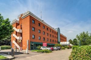 un bâtiment en briques rouges avec des voitures garées dans un parking dans l'établissement Hotel Della Rotonda, à Saronno