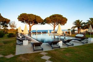 a pool with chairs and umbrellas next to the water at Resort Capo Bianco in Porto Azzurro