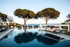 einen Pool mit Stühlen, Bäumen und Wasser in der Unterkunft Resort Capo Bianco in Porto Azzurro