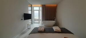 a white bathroom with a tub and a television at Porto Covo Praia Hotel & SPA in Porto Covo