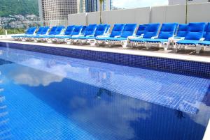 a swimming pool with blue chairs sitting next to the water at One Acapulco Costera in Acapulco