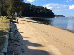 a sandy beach with a boat in the water at Currawong Beach Cottages in Great Mackerel Beach