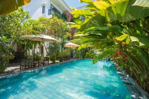 a swimming pool with chairs and umbrellas next to a building at Coco Island Villa in Hoi An