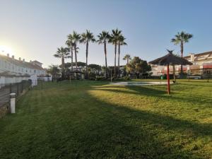 ein Grasfeld mit Palmen und einem Regenschirm in der Unterkunft Adosado de lujo en El Portil Playa y Golf in El Portil