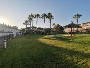 a grass field with palm trees and an umbrella at Adosado de lujo en El Portil Playa y Golf in El Portil