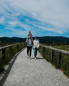 two people walking down a road with a child on their shoulders at OREA Hotel Špičák Šumava in Železná Ruda