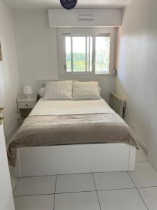 a white bedroom with a bed with a window at Vue mer et verdure in Villers-sur-Mer
