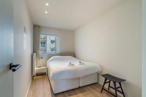 une petite chambre avec un lit blanc et un tabouret dans l'établissement Rustig, comfortabel app op 50meter van het strand, à Coxyde