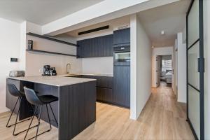 une cuisine avec des placards sombres et un îlot avec des chaises dans l'établissement Rustig, comfortabel app op 50meter van het strand, à Coxyde