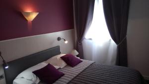 a bedroom with a bed with purple pillows and a window at Hôtel Montespan in Lussac-les-Châteaux