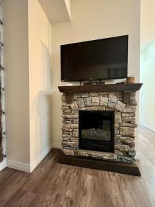 a living room with a stone fireplace with a flat screen tv at Nakiska, 2 Bed 1 Bath with Mtn Views in Canmore
