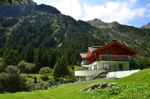 una casa en una colina con montañas en el fondo en Appartementhaus Naturquell, en Sankt Leonhard im Pitztal