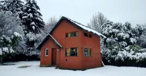 a red house in the snow with trees at La Avutarda in San Carlos de Bariloche