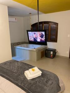 a room with a tub with a tv and a bed at Village Colonial Pousada in Penedo