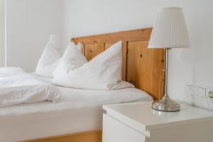 een wit bed met witte kussens en een tafel met een lamp bij MANTANA - Apartments in San Lorenzo di Sebato