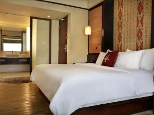 a bedroom with a large white bed and a bathroom at Novotel Lombok Resort & Villas in Kuta Lombok