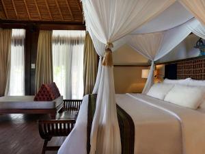 a bedroom with a canopy bed and a chair at Novotel Lombok Resort & Villas in Kuta Lombok